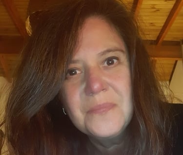 Close-up portrait of a woman with long brown hair inside a room with a rustic wooden ceiling.