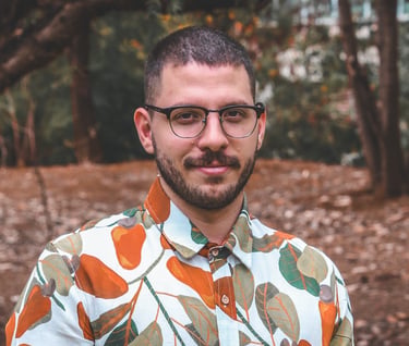 A man with glasses and a beard wearing a colorful floral print shirt outdoors in a park.
