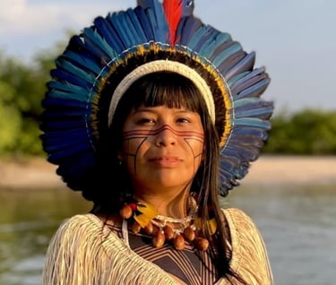 Indigenous Brazilian woman wearing a blue feather headdress and traditional facial paint by a river.