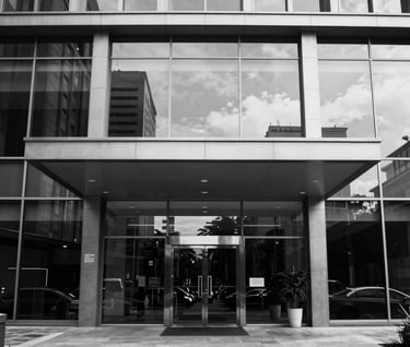 A ground-level shot of a sleek commercial building entrance in a South American / Brazilian business district. The glass reflects a clear sky. Minimalist, clean composition with a focus on negative space. Black and white aesthetic.