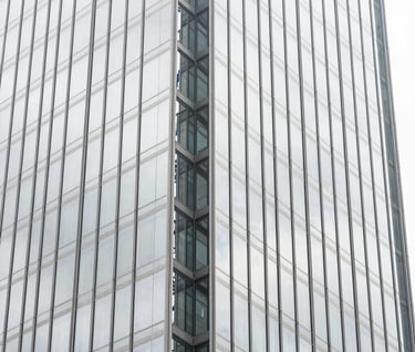 A vertical architectural photograph showing a detail of a glass and steel skyscraper in a South American / Brazilian city. The image is mostly pure white and light silver grey reflections with sharp charcoal grey geometric lines. High-end, premium mood.