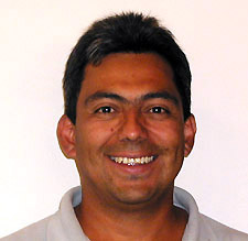 A headshot of a smiling middle-aged man with dark hair against a plain white background.