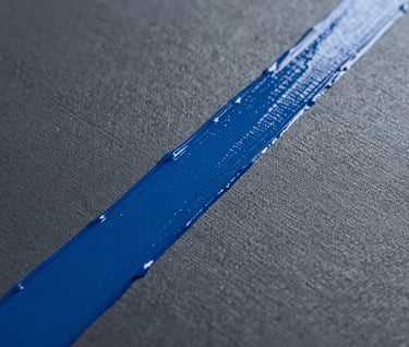 A macro shot of a canvas surface showing the intersection of matte deep slate grey paint and a glossy vibrant blue acrylic stroke. The texture of the canvas weave is visible. High-contrast, editorial photography in an International / Urban Art Scene art space.