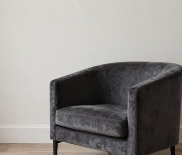 A styled corner of a modern North American / Western European living room, featuring a dark charcoal grey velvet armchair next to a soft off-white wall, minimalist and calm fashion-inspired atmosphere.