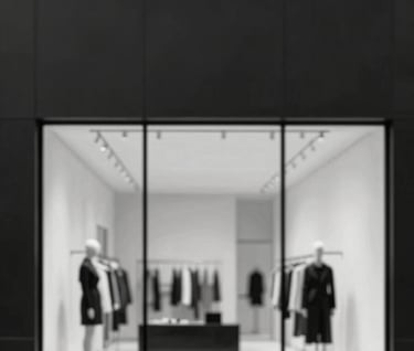 A minimalist black-and-white editorial image of a luxury retail space's exterior facade, with sharp vertical lines. The image is high-contrast, with the shadows being deep charcoal (#111111) and the highlights being warm off-white (#F0EDE8). No distracting elements, pure form.