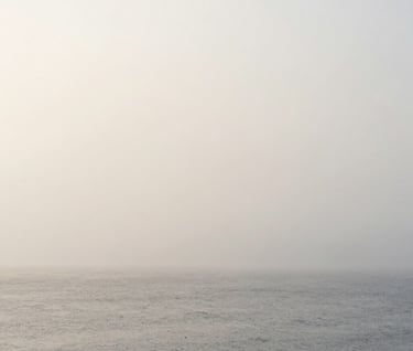 A full-width landscape photograph of a misty, minimalist horizon in Northern Europe. The sea and sky blend into a seamless field of soft light gray and off-white. Tranquil, ethereal, and deeply focused on atmospheric texture.