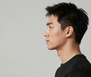 A professional studio portrait focusing on the actor's profile. Clean, minimalist aesthetic. The lighting is soft but defined, accentuating the jawline against a neutral background of #F5F5F5 and #333333. Refined and artistic mood.