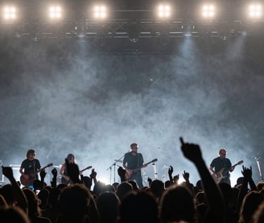 An action shot from a North American concert, showing a crowd silhouette against a dark gray and silver light show. The scene captures a high-energy, professional musical performance vibe.