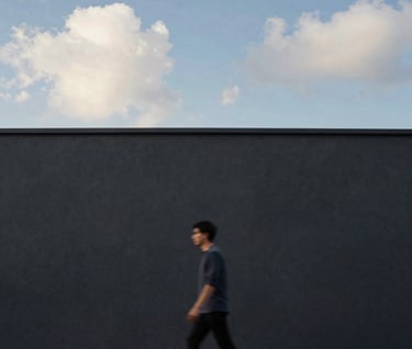 A medium shot of a solitary figure walking past a deep charcoal wall. The person is blurred slightly to suggest motion, while the architectural background remains in sharp, elegant focus. Tones of steel blue and soft cloud white dominate.