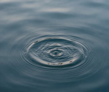 An abstract close-up of water ripples in a slate blue pool, reflecting mist grey light. The composition is clean, calm, and highly professional.