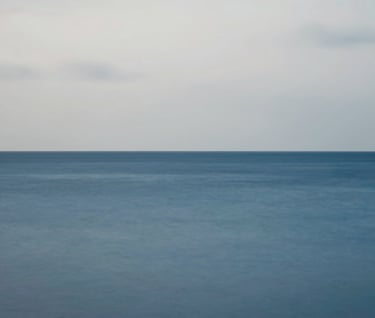 A minimalist landscape featuring a Steel Blue horizon where the sea meets a Pale Grey sky, captured with a long exposure for a smooth, immersive texture.
