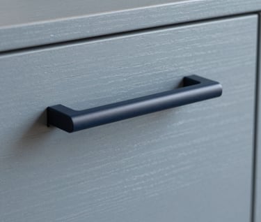 Close-up of a minimalist custom cabinet handle, sophisticated Dark Navy matte finish against a Soft Gray Blue wood surface. Elegant and precise, minimalist Northern European furniture design.