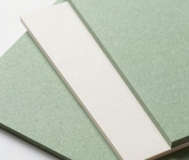 Macro photography of high-quality sustainable paper stocks. The textures are varied, showing a mix of soft sage green and mist white cardstock. Bright, clean studio lighting in a North American / US design workspace.
