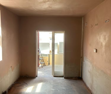 In the empty room under renovation, the walls have been freshly plastered and the concrete subfloor