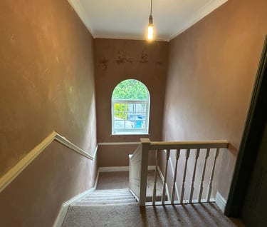 A carpeted staircase renovation with dusty pink walls, white banisters, and an arched window.