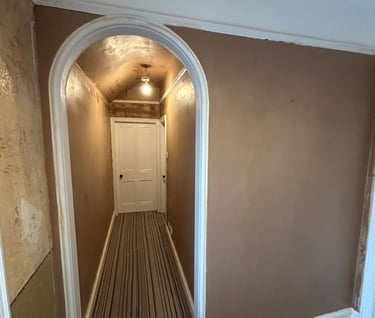 Freshly plastered brown walls and arched doorway in a home renovation hallway with striped carpet.