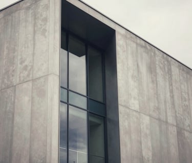 An artistic architectural detail of a contemporary European / French museum exterior. The structure is made of silver grey metal and glass, reflecting a soft off-white sky. The composition is clean, modern, and timeless.