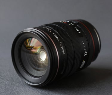 A refined shot of a professional camera lens on a dark gray surface, catching a sliver of bright white light, cinematic and technical, representing high-end expertise, Global / Hispano style.