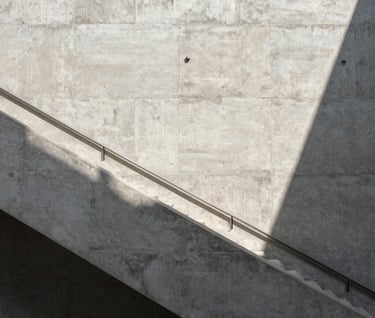 An architectural view of a concrete staircase in a modern North American / European museum. The shot is high-angle, emphasizing the repetitive geometry and the play of light and shadow in shades of light gray and white.