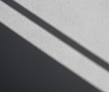A study of geometric shadows cast across a textured light gray wall, sharp diagonal lines, high contrast monochromatic photography, minimalist and balanced composition, North American / European.