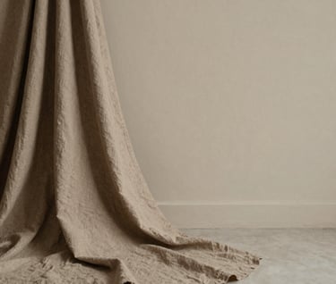 An intimate portrait shot in an airy room with soft linen textures. The subject is draped in a warm taupe fabric, creating a serene and sophisticated mood. Minimalist composition with plenty of negative space.