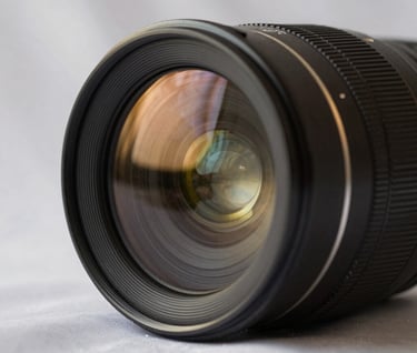 A macro photograph of a high-end camera lens reflecting soft silk off-white studio lights, with subtle muted metallic gold highlights on the lens housing.