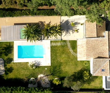 Vue aérienne d'une villa de luxe avec une piscine turquoise, pelouse verte manucurée et palmiers.