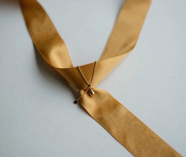 An artistic close-up of a bride's wedding accessories, including delicate gold jewelry and a mustard yellow silk ribbon. Shot against a light grey professional studio backdrop. Minimalist and elegant composition.