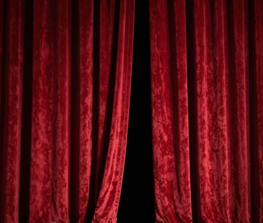 A cinematic shot of a theater's red velvet curtains slightly parted, with soft light spilling from the stage. The colors are deep red and dark gray. North American / US theater architecture.