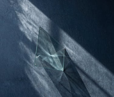 Abstract photography of light filtering through a glass installation, creating poetic shadows on a dark slate blue wall, minimalist and avant-garde style, Latinoamericano / Español context.