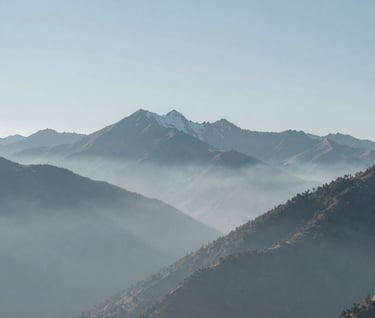 A serene, minimalist landscape of the high-altitude Andes mountains in a Latinoamericano / Español region, captured in muted tones of blue and gray, soft fog rolling between peaks, very clean and artistic composition.