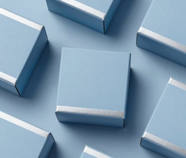 A top-down flat lay of minimalist spirits packaging prototypes. The boxes are made from sustainable matte paper in #ECF0F1 with subtle silver foiling. The composition is balanced and architectural, emphasizing a clean, cutting-edge design aesthetic.