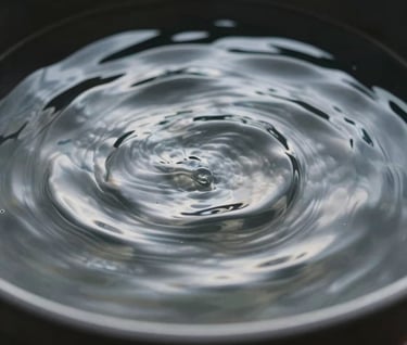 Abstract photography showing water ripples in a dark charcoal black basin. The peaks of the waves catch a soft cloud white light, creating a shimmering muted steel effect. Minimalist and calm.