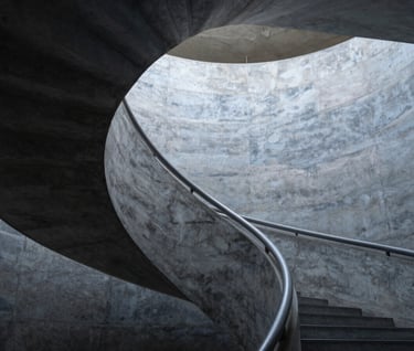 A vertical shot of a spiral staircase in a modern museum. The Charcoal Blue shadows and Dusty Slate concrete textures create a sense of infinite rhythm and depth.