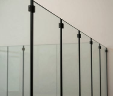 Architectural perspective view of a series of glass panels held by minimalist black steel mullions. The composition emphasizes technical precision and linear geometry, with soft off-white walls in the background.