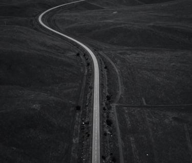An aerial view of a winding road through a minimalist landscape, monochromatic dark gray tones, crisp lines and elegant composition, North American / US setting.