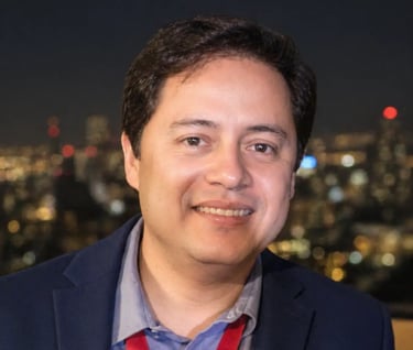 A dark hair guy with blue suit, smiling, named Albert Serrano, with a lighted city on his back