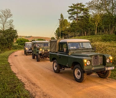 a group of three classic land rovers driving down a dirt road