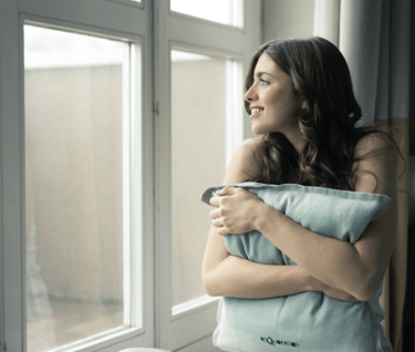a girl sitting beside window and holding pillow