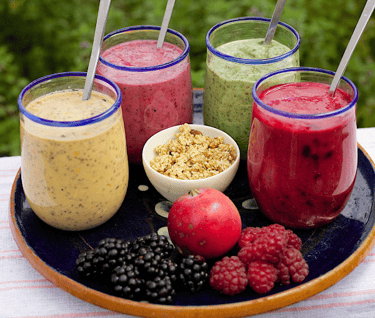 four smoothie glasses in tray with some fruits