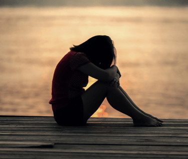 a sad girl sitting on near sea