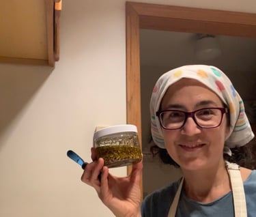 Katrina Matos with bandana covering hair, & holding up a jar of herb-infused oil