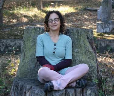 Katrina Matos sitting on tree trunk, slightly smiling, eyes closed