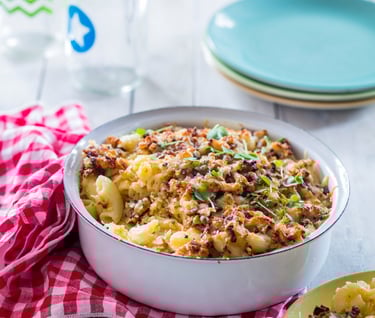 Mac and Cheese in a tin bowl with a crunchy topping and a checked napkin to the side
