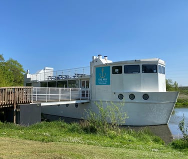 a large white boat, the ark northampton, sits in the river nene on a sunny day