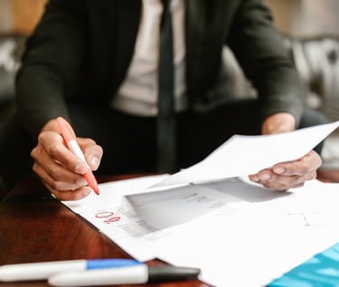 A man in a suite at his desk, writing on financial papers with a red marker