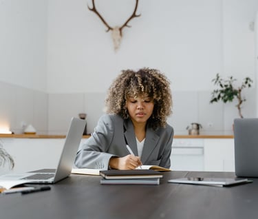 Black woman sitting at a desk and writing in a notebook 