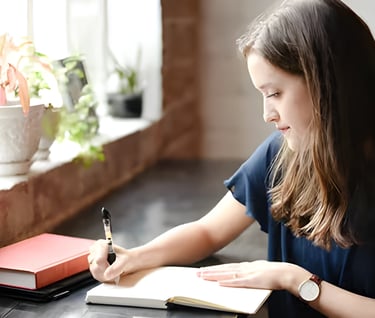 Young woman writing at a desk, symbolizing personalized guidance in crafting compelling SoPs and LOR