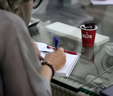 Person writing in a notebook, symbolizing IELTS preparation with U.E.L.T's cup for studying abroad