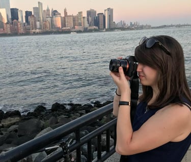 A woman holding a camera pointed toward the New York City skyline
